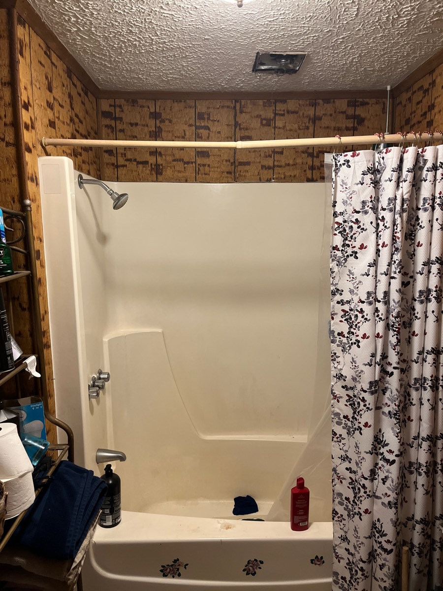 Bathroom before remodel — dated fiberglass tub and wood paneling