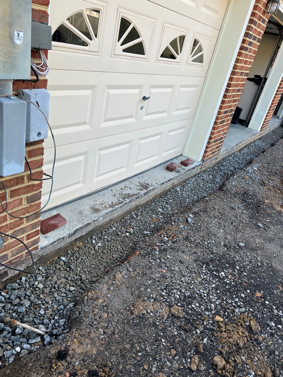 Driveway before — excavated gravel trench along the garage apron