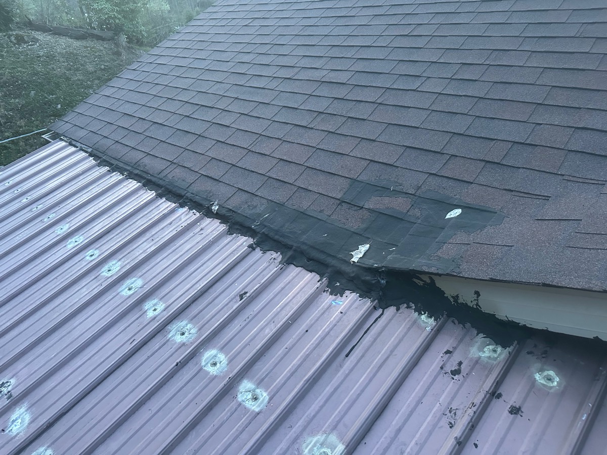Roof before repair — failed tar-patched transition where shingles meet metal porch roof